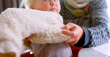 Beyaz babanın orta kesimi kızına evde kazak takmasına yardım ediyor. Masada oturuyorlar. 4k