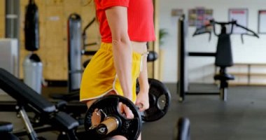 Bir fitness stüdyosunda barbell ile egzersiz Kafkas kadının yan görünümü. Çömelmiş gibi yapıyor. 4k