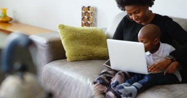 Rahat bir evde dizüstü bilgisayar kullanarak Afrikalı Amerikalı anne ve oğlu Ön görünümü. Kanepede oturuyorlar. 4k