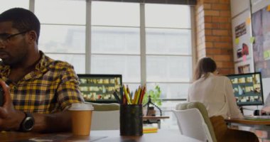 Masabaşında dijital fotoğraf makinesifotoğrafları gözden Afrikalı Amerikalı Amerikalı erkek grafik tasarımcı ön görünümü. Arka planda çalışan kadın meslektaşım. 4k