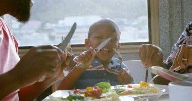 Rahat bir evde yemek masasında yemek olan gülümseyen Afrikalı-Amerikalı aile ön görünümü. 4k