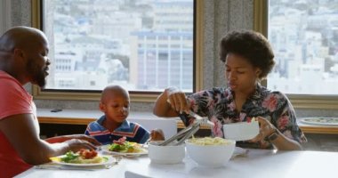Afro-Amerikan ailenin rahat bir evde yemek masasında yemek yemesi ön planda. Annem yemek servisi yapıyor. 4k