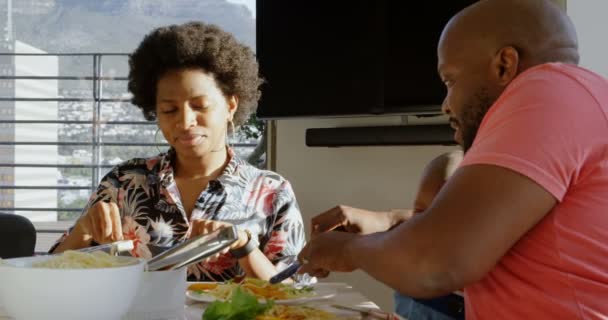 非洲裔美国父亲在餐桌上教儿子用叉子和刀子吃饭的侧视图 妈妈看着他们4K — 图库视频影像