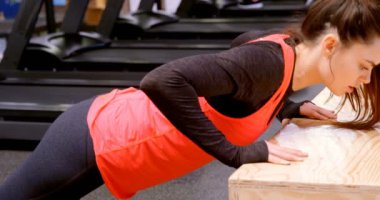 Fitness stüdyosunda ahşap kutu üzerinde şınav yapıyor kararlı güzel Kafkas kadın yan görünümü. Kararlı ve odaklanmış durumda. 4k