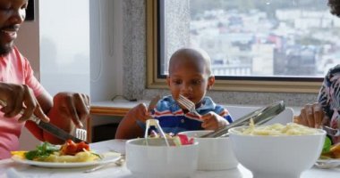 Rahat bir evde yemek masasında yemek olan Afrikalı-Amerikalı ailenin ön görünümü. Çatal bıçak kullanıyorlar. 4k