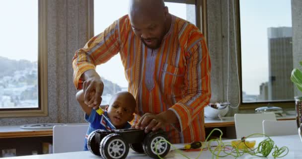 前视图的非洲裔美国人的父亲和他的儿子在一个舒适的家庭修理玩具车 他们正在使用螺丝刀 — 图库视频影像