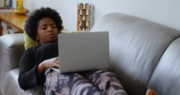 快適な家のソファでラップトップを使用してアフリカ系アメリカ人女性の正面図 彼女はソファに横たわっている — ストック動画