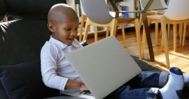 Rahat bir evde dizüstü bilgisayar kullanarak gülümseyen Afrikalı Amerikalı çocuk Yan görünümü. 4k