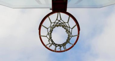 Basketbol sahasında basketbol potası geçiyor Yukarı görünümü. Arka planda gökyüzü ve bulutlar 4k