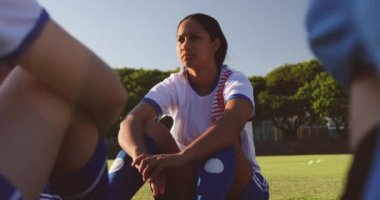 Karışık ırk kadın futbolcu futbol sahasında takım arkadaşı yanında yerde oturan ön görünümü. 4k