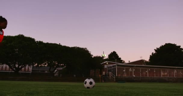在夕阳下 穿着橙色背心的非洲裔美国女足球员在足球场上射门 — 图库视频影像