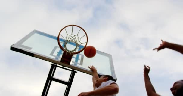 バスケットボールコートでバスケットボールをしている多民族バスケットボール選手の低角度ビュー 4Kでゴールを決める — ストック動画