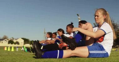 Güneşli bir günde futbol sahasında antrenman öncesi bacaklarını geren çeşitli kadın futbol takımının yan görünümü. 4k