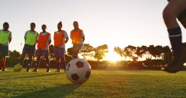 一名女足球员射门的侧视图 而不同的女子足球队在黄色和橙色背心站在足球场上 — 图库视频影像