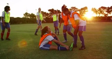 Afro-Amerikan kadın futbolcunun futbol sahasında durması için yaralı Kafkas kadın takım arkadaşına yardım etmesi ön görünümü. 4k