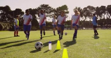 Güneşli bir günde futbol sahasında kardiyo egzersizleri yapan çeşitli kadın futbol takımı ön görünümü. 4k