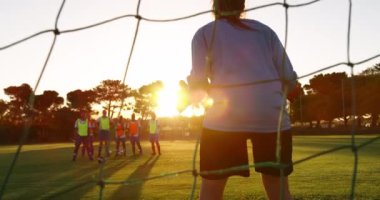 Kafkas kadın kalecinin arka dansı topu durdurmaya çalışırken, farklı kadın futbol takımı ise sarı-turuncu yeleklerle futbol sahasında ayakta duruyor. 4k