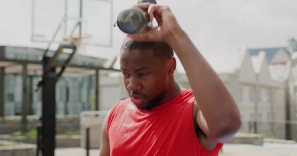バスケットボールコートで頭に水を注ぐアフリカ系アメリカ人バスケットボール選手の正面図 彼は疲れて疲れている4K — ストック動画