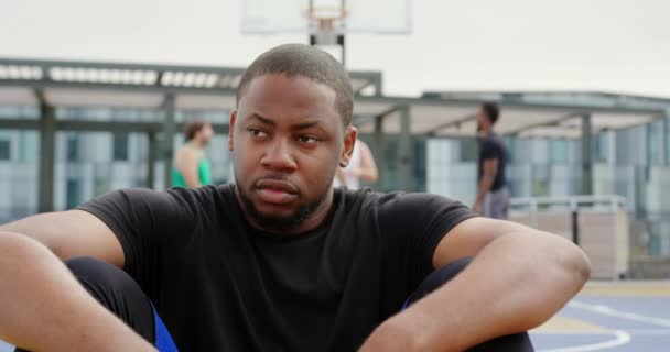 坐在篮球场上非洲裔美国篮球运动员的正面观 他心烦意乱 望向远方4K — 图库视频影像