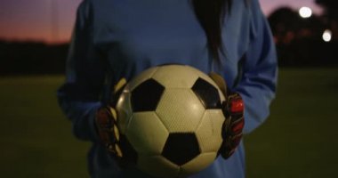 Mutlu Kafkas kadın futbolcu portresi gece futbol sahasında topu tutarken gülümseyen. 4k