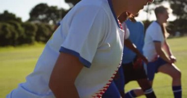 Güneşli bir günde futbol sahasında bacaklarını geren konsantre çeşitli kadın futbolcuların yan görünümü. 4k