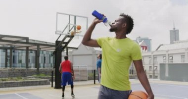 Basketbol sahasında su içen Afrikalı-Amerikalı basketbolcu ön görünümü. O gülümsüyor ve kamera 4k bakıyor