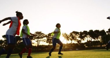 Karışık Yarış kadın oyuncu gün batımında futbol sahasında kafa ile topa vururken çeşitli kadın futbol takımı eğitim yan görünümü. 4k