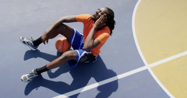 コートでバスケットボールを着て座っているアフリカ系アメリカ人バスケットボール選手の高角図 彼は疲れている4K — ストック動画