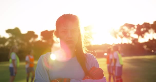 チームメイトがサッカー場で彼女の後ろでサッカーをしている間 腕を組んで立っている白人女性サッカー選手の肖像画 — ストック動画