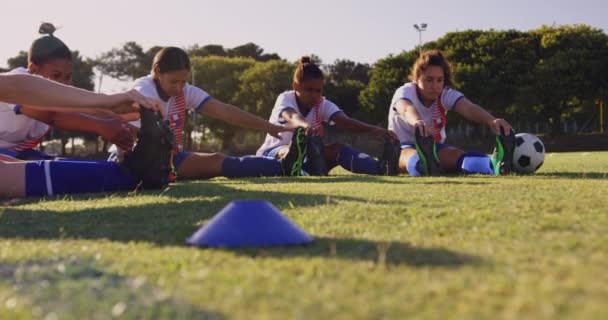 在阳光明媚的日子里 不同的女足球员坐在地上 在足球场上摸着脚趾 — 图库视频影像