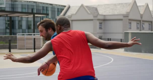 バスケットボールコートでバスケットボールをしている多民族バスケットボール選手の背面図 彼らはバスケットボール4Kをかわしている — ストック動画