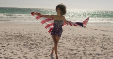 Sahilde Amerikan bayrağıyla koşan Afrikalı-Amerikalı kadının yan görünümü. O 4k gülümsüyor