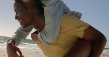 Sahilde ki kadına domuz sırtı süren Afro-Amerikan erkeğin yan görünümü. Onlar gülümsüyor ve eğleniyor4k