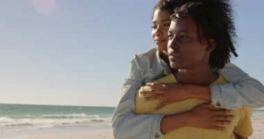 Sahilde kadına piggyback sürüş veren Afrikalı Amerikalı adam ön görünümü. Onlar uzak 4k arıyoruz