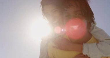 Sahilde kadın piggyback sürüş veren Afrikalı Amerikalı adam düşük açı görünümü. Onlar gülümsüyor ve kamera 4k bakıyor