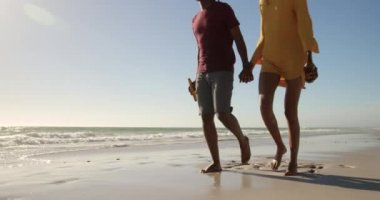 Sahilde birlikte yürüyen Afrikalı-Amerikalı çiftin ön görünümü. El ele tutuşuyorlar 4k