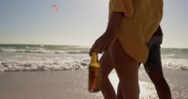 Afrikalı Amerikalı çiftin orta bölümünde sahilde birlikte yürüyorlar. El ele tutuşuyorlar 4k