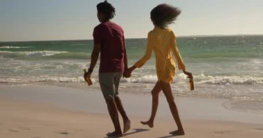 Sahilde birlikte yürüyen Afro-Amerikan çiftin arka manzarası. El ele tutuşuyorlar 4k