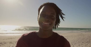 Sahilde duran Afro-Amerikan adamın ön görünümü. O gülümsüyor ve kamera 4k bakıyor