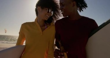 Sahilde sörf tahtası ile birlikte yürüyen Afrikalı-Amerikalı çift ön görünümü. Bira 4k içiyorlar.