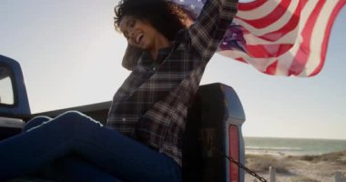Bir kamyonette Amerikan bayrağı sallayarak oturan Afrikalı-Amerikalı kadının ön görünümü. O 4k gülümsüyor