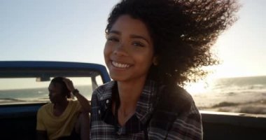 Sahilde kamyonetin yanında duran Afro-Amerikalı kadının ön görünümü. Adam arka planda 4k pikap kamyon üzerinde rahatlatıcı