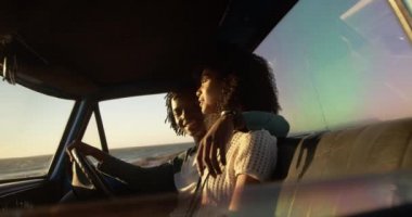 Bir plajda kamyonetle birlikte oturan Afrikalı-Amerikalı çiftin yan görünümü. Onlar gülümsüyor ve 4k konuşuyor