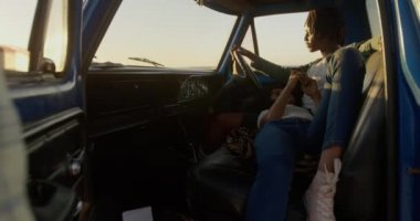 Sahilde bir kamyonette erkek kucağında yatan Afrikalı-Amerikalı kadının ön görünümü. O cep telefonu 4k kullanıyor