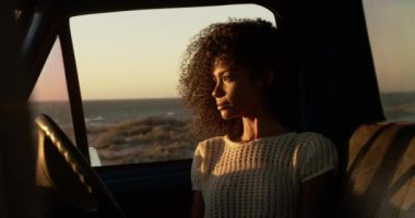 Sahilde kamyonette oturan Afrikalı-Amerikalı kadının ön görünümü. O 4k uzağa bakıyor