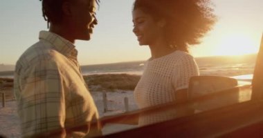 Sahilde kamyonetin yanında birbirlerine kucak layan Afrikalı-Amerikalı çiftin yan görünümü. Onlar 4k gülümsüyor