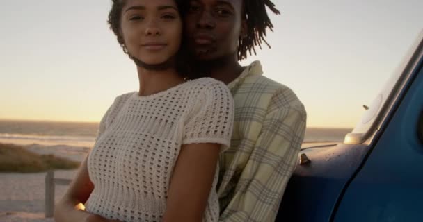 ビーチでピックアップトラックの近くに女性を抱きしめるアフリカ系アメリカ人男性の正面図 彼らはカメラ4Kを見ている — ストック動画
