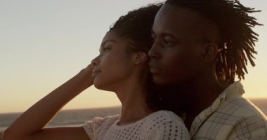 Gün batımında plajda kadını kucaklayan Afrikalı-Amerikalı erkeğin yan görünümü. Onlar uzak 4k arıyoruz