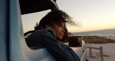 Sahilde kamyonetin camına yaslanmış Afrikalı Amerikalı kadının yan görünümü. O düşünceli ve uzak 4k bakıyor