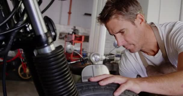 白种男性机械师在修理车库修理摩托车的前视图 他正在修理摩托车车轮4K — 图库视频影像